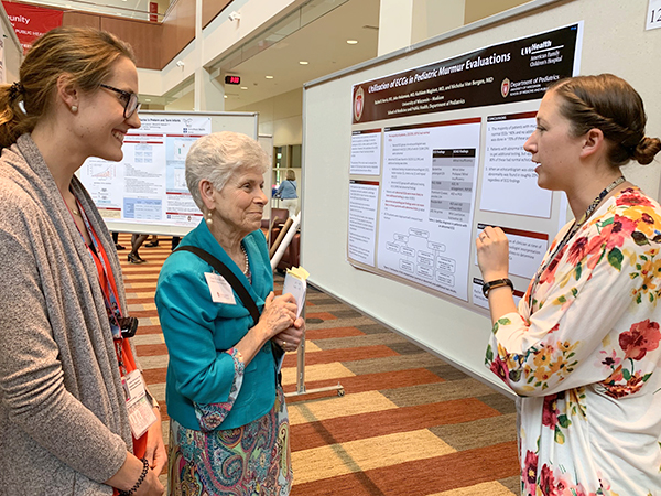 Resident Lindsay McGowan, MD (on left), listens in while resident Rachel Harris, DO (on right), discusses her poster on use of ECG in pediatric murmur evaluation with Department of Pediatrics Chair Ellen Wald, MD.