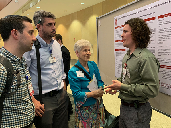 Resident Nicholas Beam, MD, and UW School of Medicine and Public Health student Patrick O’Donnell (on left) listen as resident Dane Hammer, MD (on right), discusses his poster on diuresis for adolescents hospitalized for severe eating disorders with Department of Pediatrics Chair Ellen Wald, MD.