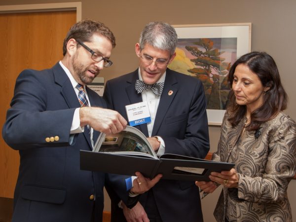 Dr. Ross (on left) reviews a photo book of the new emergency department with James Berbee, MD, MS, MBA, a clinical assistant professor in the BerbeeWalsh Department of Emergency Medicine, and Azita Hamedani, MD, MPH, MBA, who chairs that department.