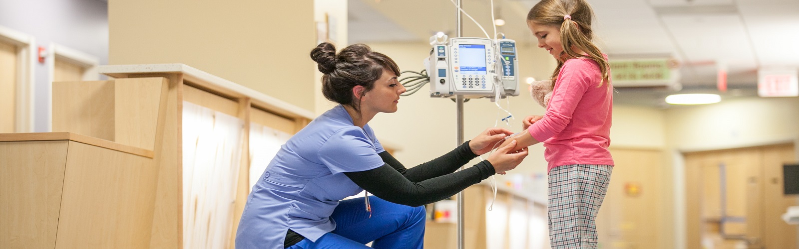 young patient walking with an IV and a nurse checking it