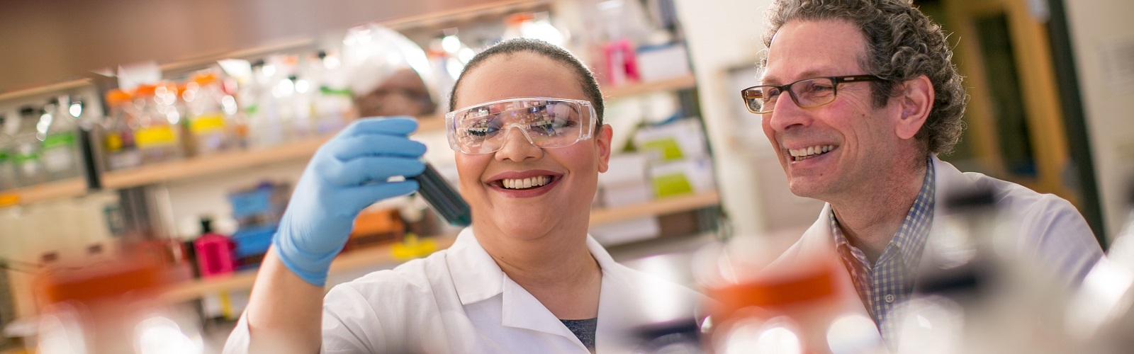 two researchers smiling in a lab, looking at a test tube