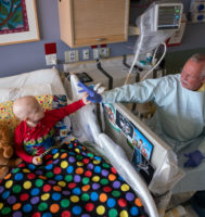 parent holding the hand of a child in a hosptial bed