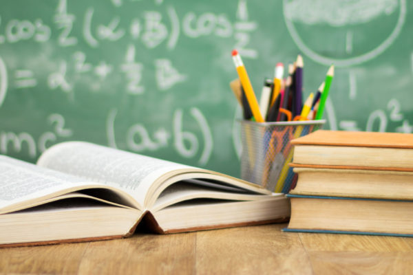 books on a desk in front of a green chalkboard with algebra equations