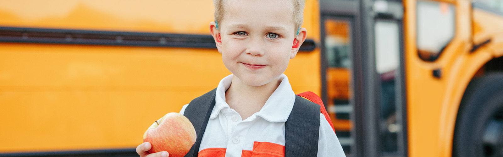boy with apple standing in front of school bus