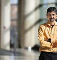 Dr. Vivek Balasubrameniam standing in an indoor atrium and wearing a yellow shirt