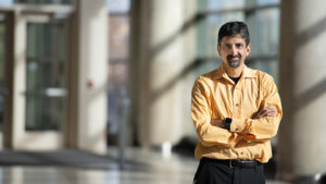 Dr. Vivek Balasubramaniam standing in an indoor atrium and wearing a yellow shirt
