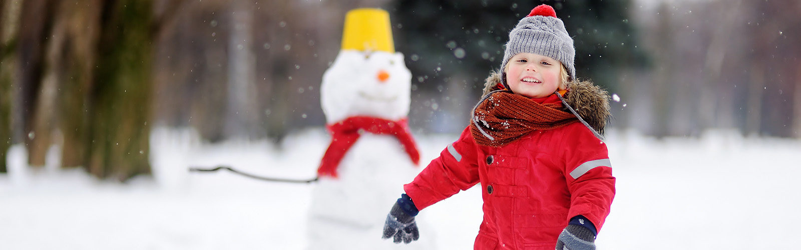 child dressed in red snowsuit running toward camera with snowman in background