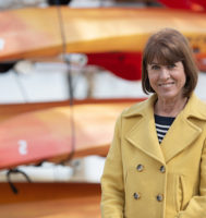 Ann Dodge standing outside in a yellow coat in front of a rack of kayaks