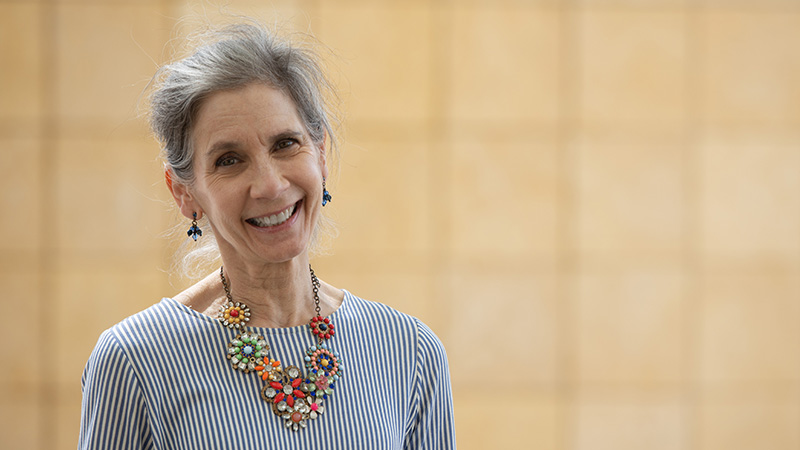 Woman smiling at the camera wearing a striped shirt and a colorful flower necklace