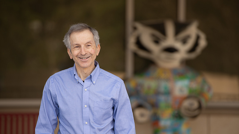 Man wearing blue Oxford shirt standing in front of a colorful Bucky Badger statue in the background