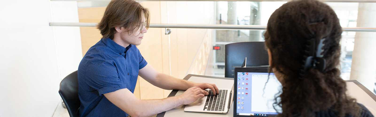 two college-aged students working at a table on laptop computers