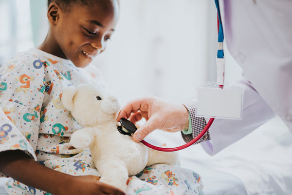 child holding teddy bear while doctor checks the teddy bear's chest with a stethoscope