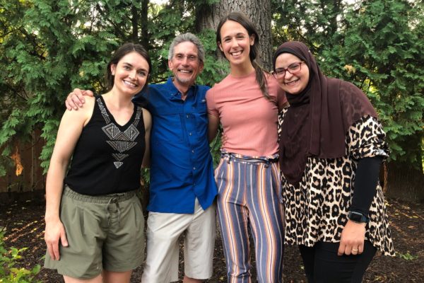 three women and one man standing side by side, smiling, in front of a large tree