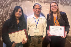 Two people holding award certificates with a third person in the middle