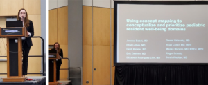 woman standing at podium giving presentation next to a large screen