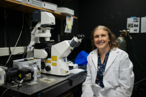 scientist wearing a lab coat sitting in front of a microscope