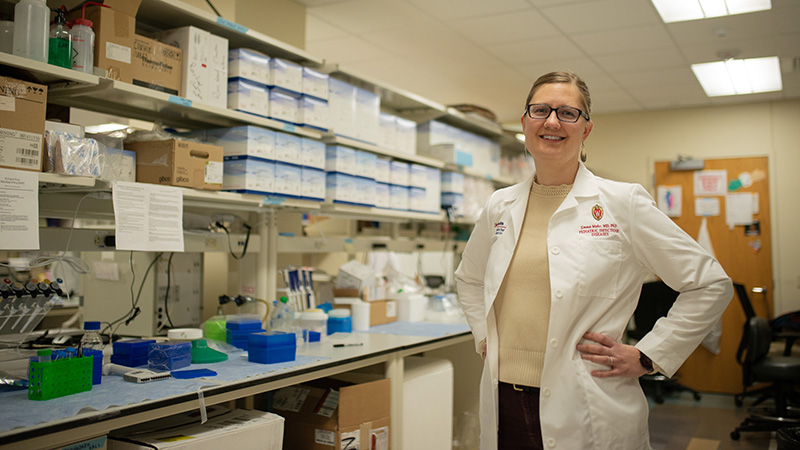 Scientist standing in a lab wearing a white lab coat and smiling at the camera