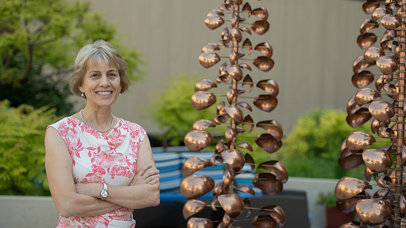 Woman standing in outdoor garden next to brass rotating wind ornaments