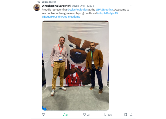Two men standing next to an image of Bucky Badger
