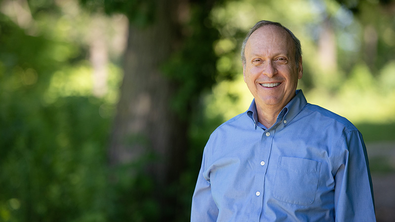 Man standing outside in a blue button-up shirt smiling at the camera