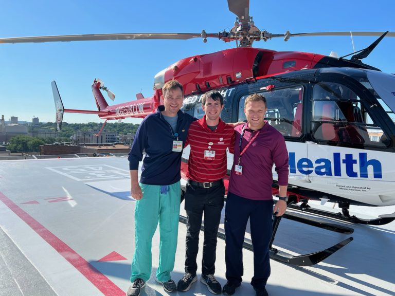 three fellows standing in front of the MedFlight helicopter, landed on a helipad on the roof of the hospital