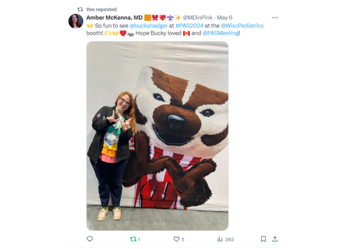 A woman with her hands making a W in front of Bucky Badger