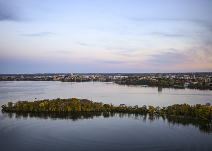 The Madison isthmus and Wisconsin State Capitol are pictured in an aerial view across Picnic Point and Lake Mendota at sunset on Oct. 22, 2023. The aerial photograph was made from a helicopter looking east. (Photo by Jeff Miller / UW–Madison)