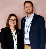 Two people standing in a conference room smiling at the camera.