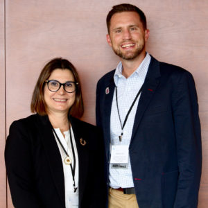 Two people standing in a conference room smiling at the camera.
