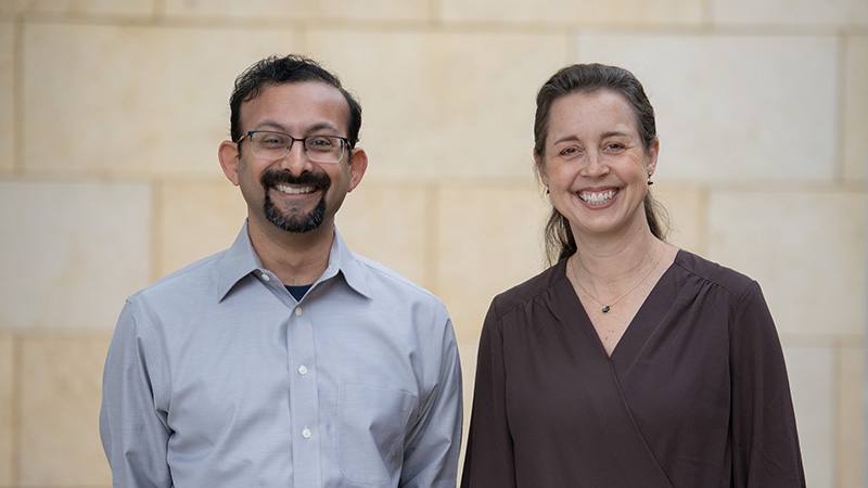 Two people standing against a wall and smiling at the camera.