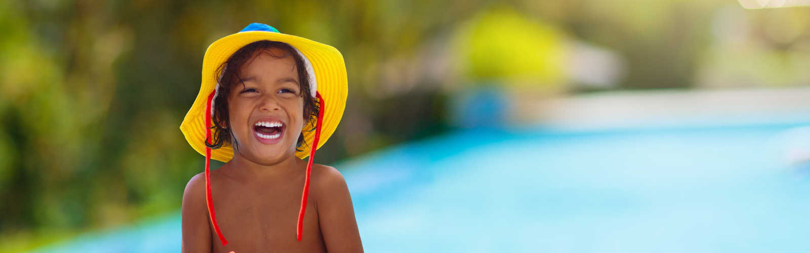 Child in a yellow sunhat smiling in front of the water