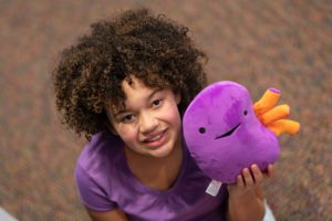 Young girl holding a purple and orange stuffed cartoon kidney.