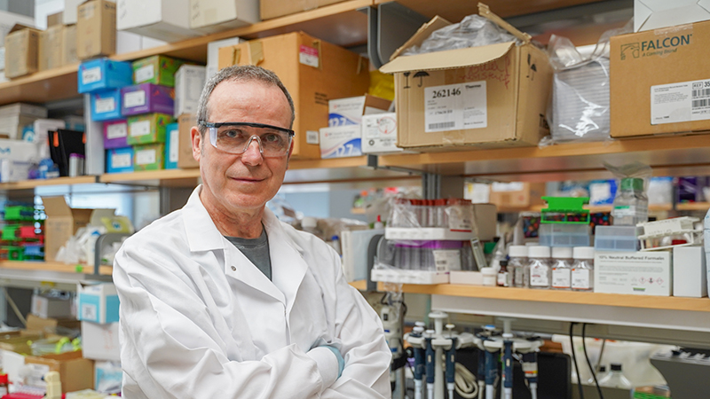 Man standing in a scientific lab wearing a white coat and protective glasses.