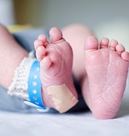 Newborn baby feet with a Band-Aid on one heel.