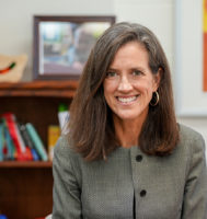 Medical researcher wearing a gray jacket, smiling at the camera, and sitting in a children's clinic area.