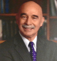 Person posing for a photo in front of a bookshelf, wearing a suit jacket and purple polka dot tie.