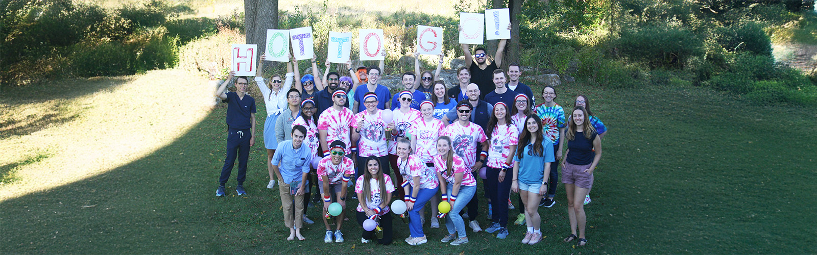 Group of people in a park wearing tie-dyed shorts and holding a sign that says "hot to go."