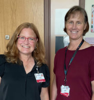 Two people standing in health care clinic setting looking at the camera and smiling.