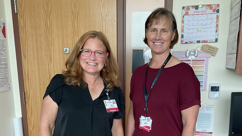 Two people standing in health care clinic setting looking at the camera and smiling.