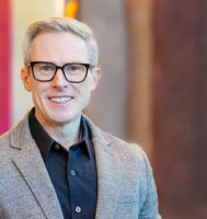 Dr. Daniel O'Connell wears a gray suit jacket and smiles at the camera.