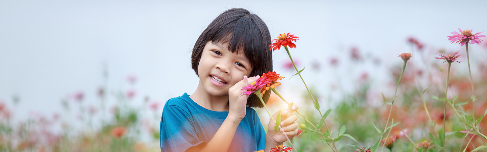 A young girl standing in a field of colorful flowers smiling into the camera