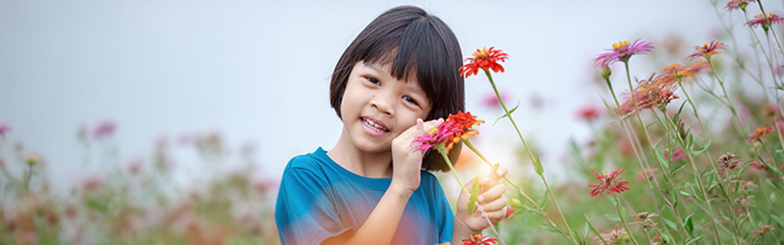 A young girl standing in a field of colorful flowers smiling into the camera