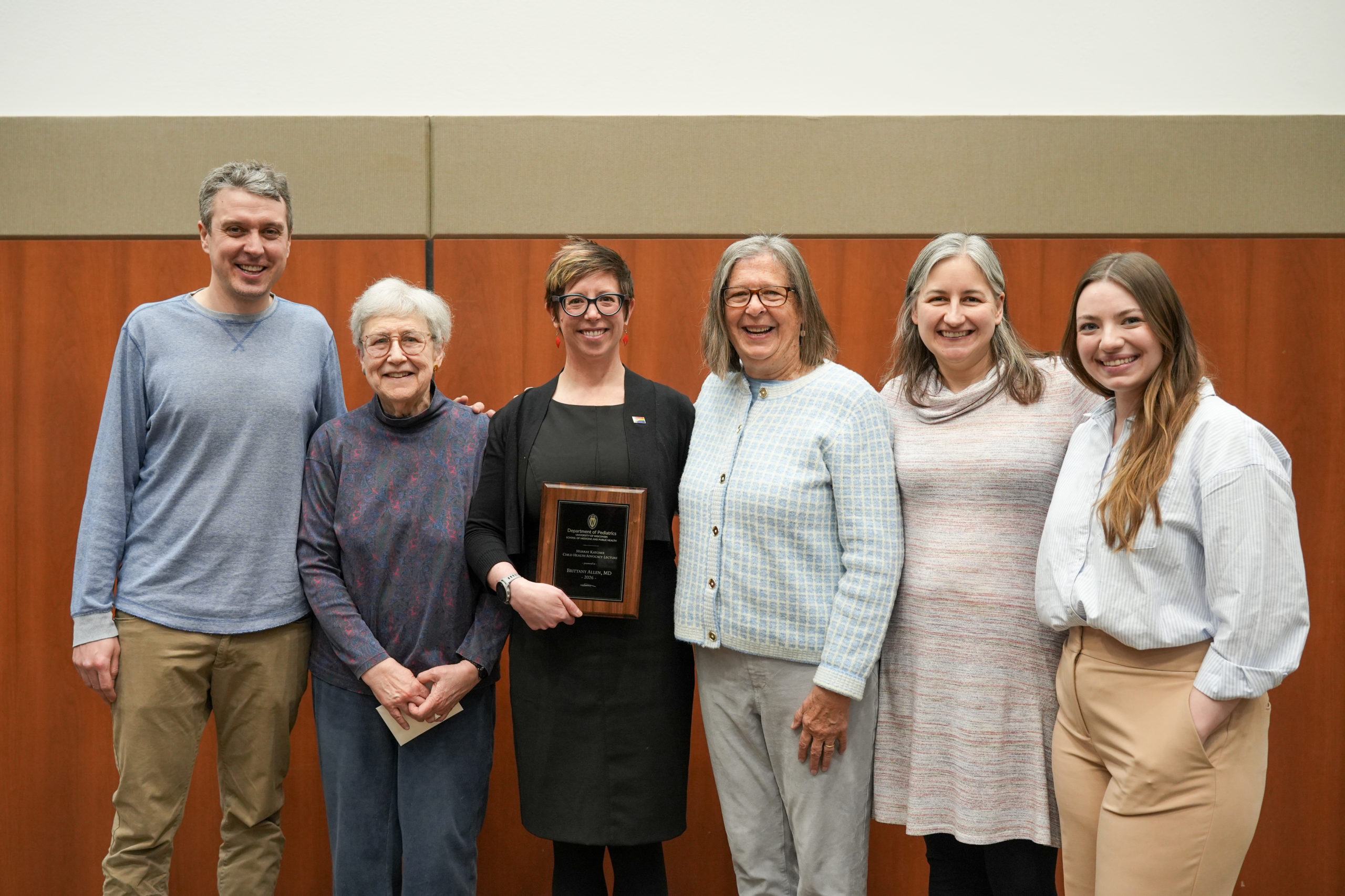 Six people posing together. One of them holds an award plaque for the Murray Katcher Child Health Advocacy Lecture.