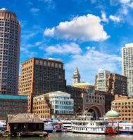 Boston, Massachusetts skyline from the water including a blue sky with white clouds and a boat.