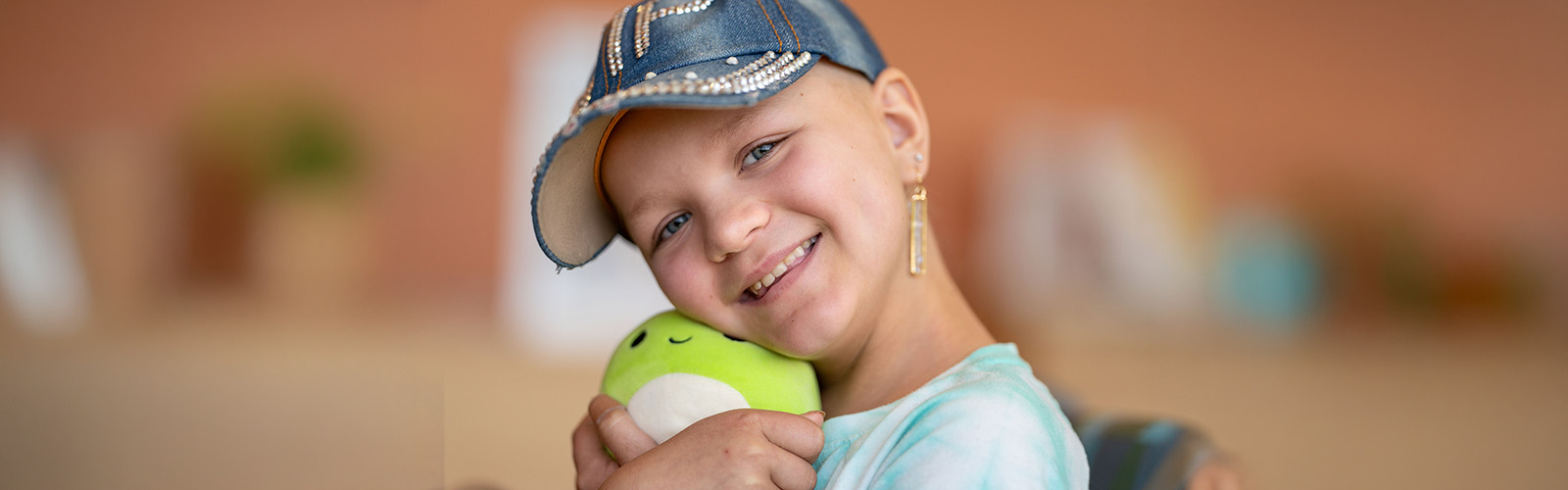 Girl wearing a bedazzled baseball cap and hugging a stuffie.