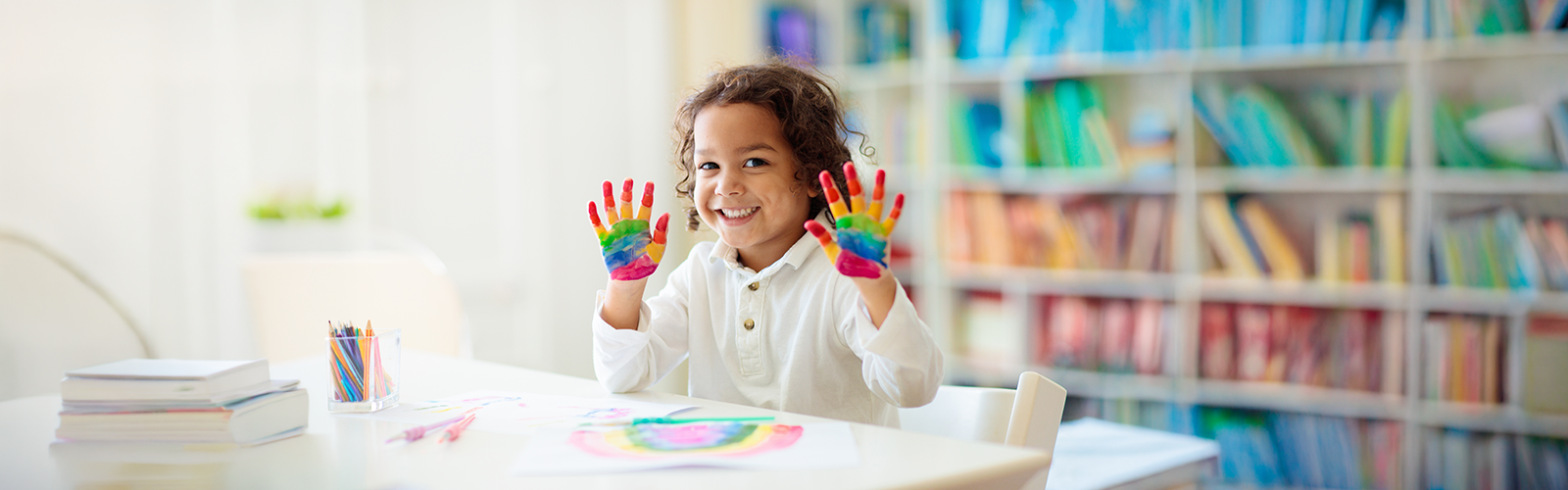Child smiling while showing her hands painted in rainbow colors.