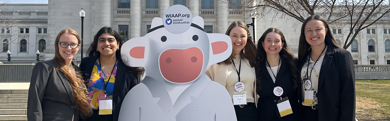 Pediatrics residents posing with a cardboard cutout of a cow dressed up as a doctor.
