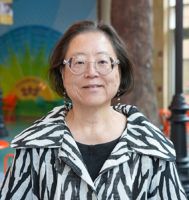 Dr. Katryn Furuya wearing a black and white print shirt with the American Family Children's Hospital atrium in the background.