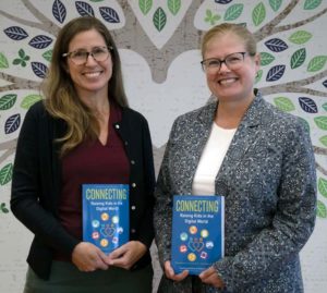 Two women holding books and smiling at the camera.