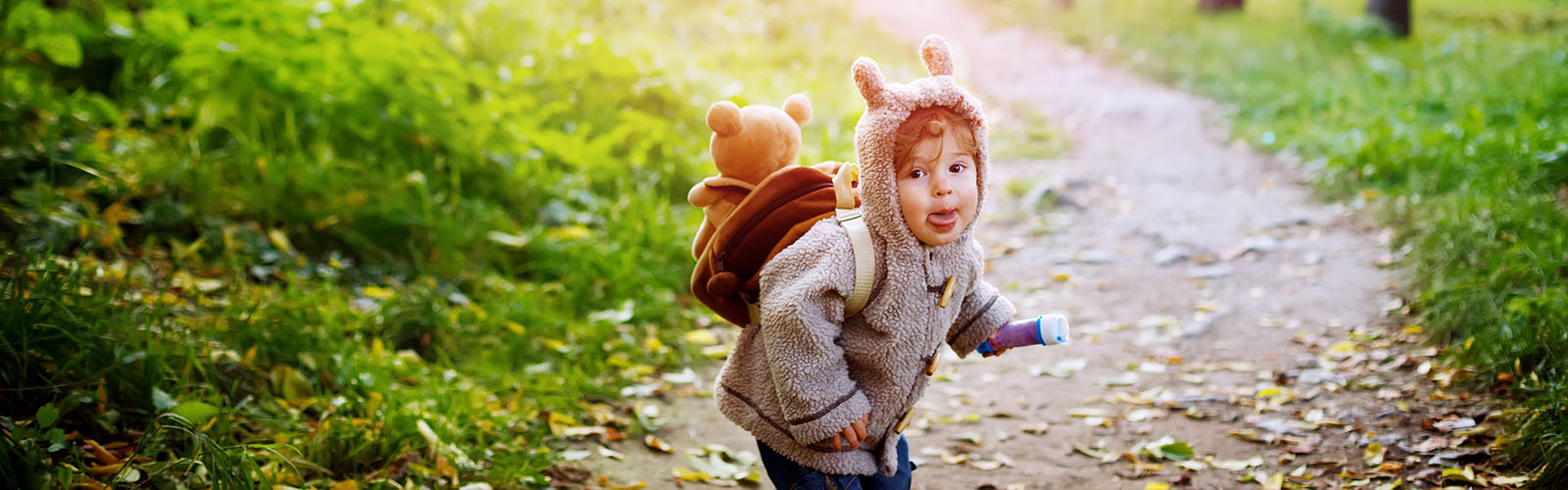 Child wearing a hooded sweatshirt with ears on a nature trail in fall.